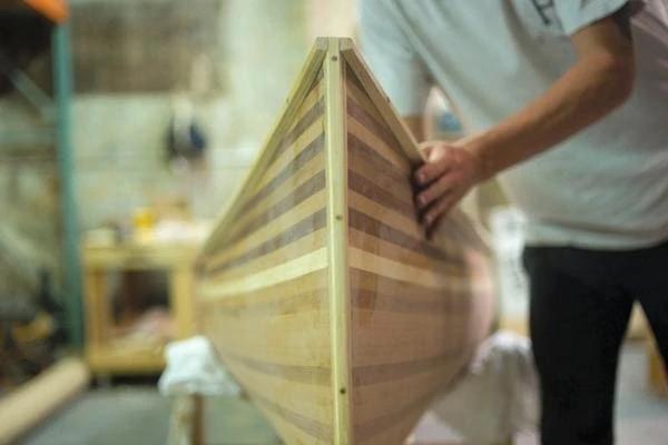 A man checks inside a nearly finished wooden canoe